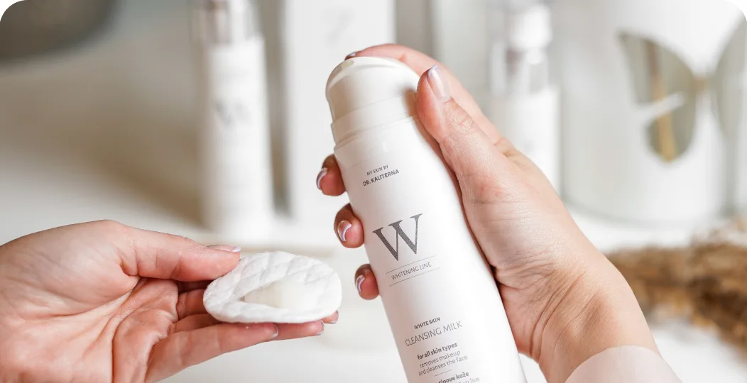 Hand holding a cleansing milk bottle and a cotton pad